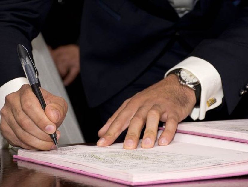 Un hombre con traje está firmando un documento con un bolígrafo.