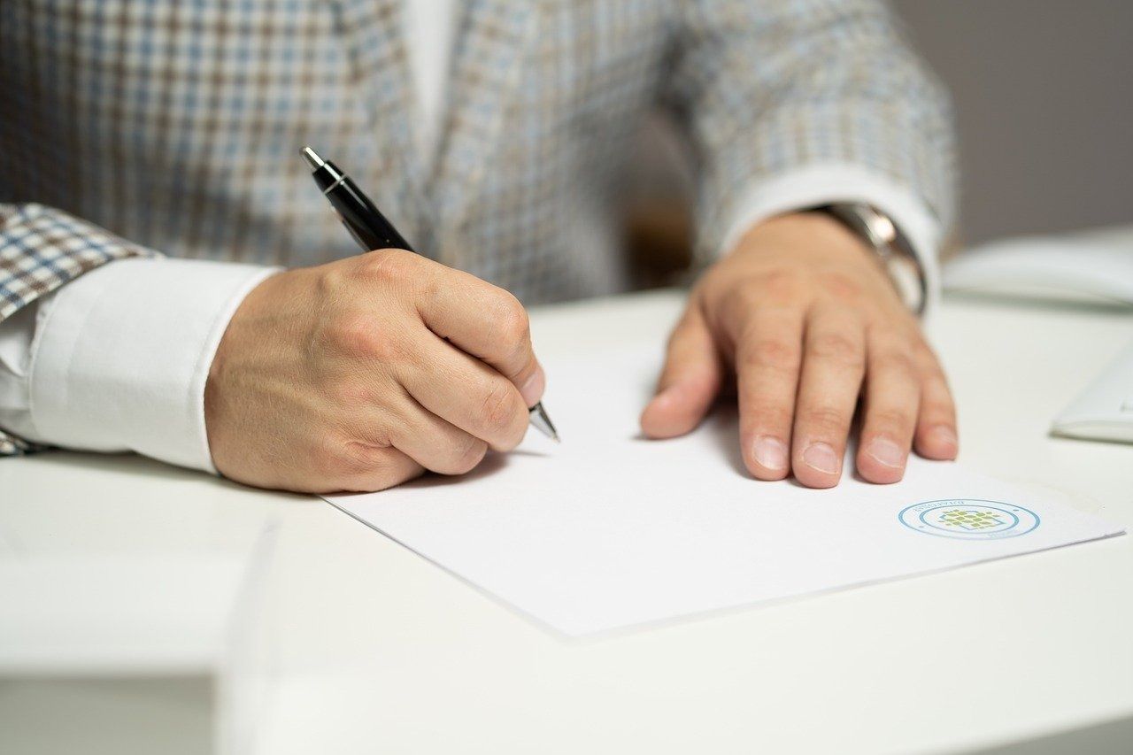Un hombre está escribiendo en un trozo de papel con un bolígrafo.