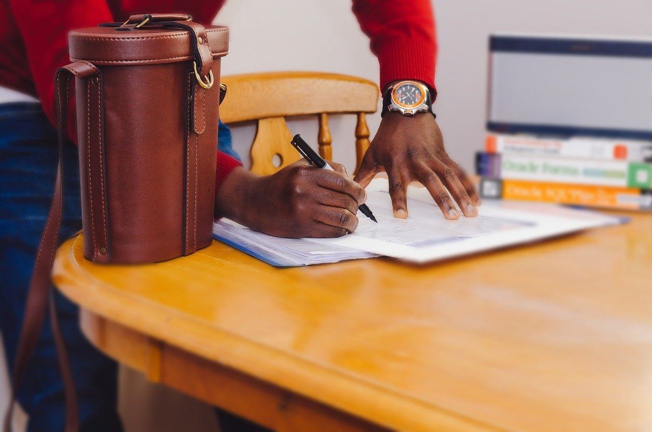 Una persona está sentada en una mesa escribiendo en un cuaderno.