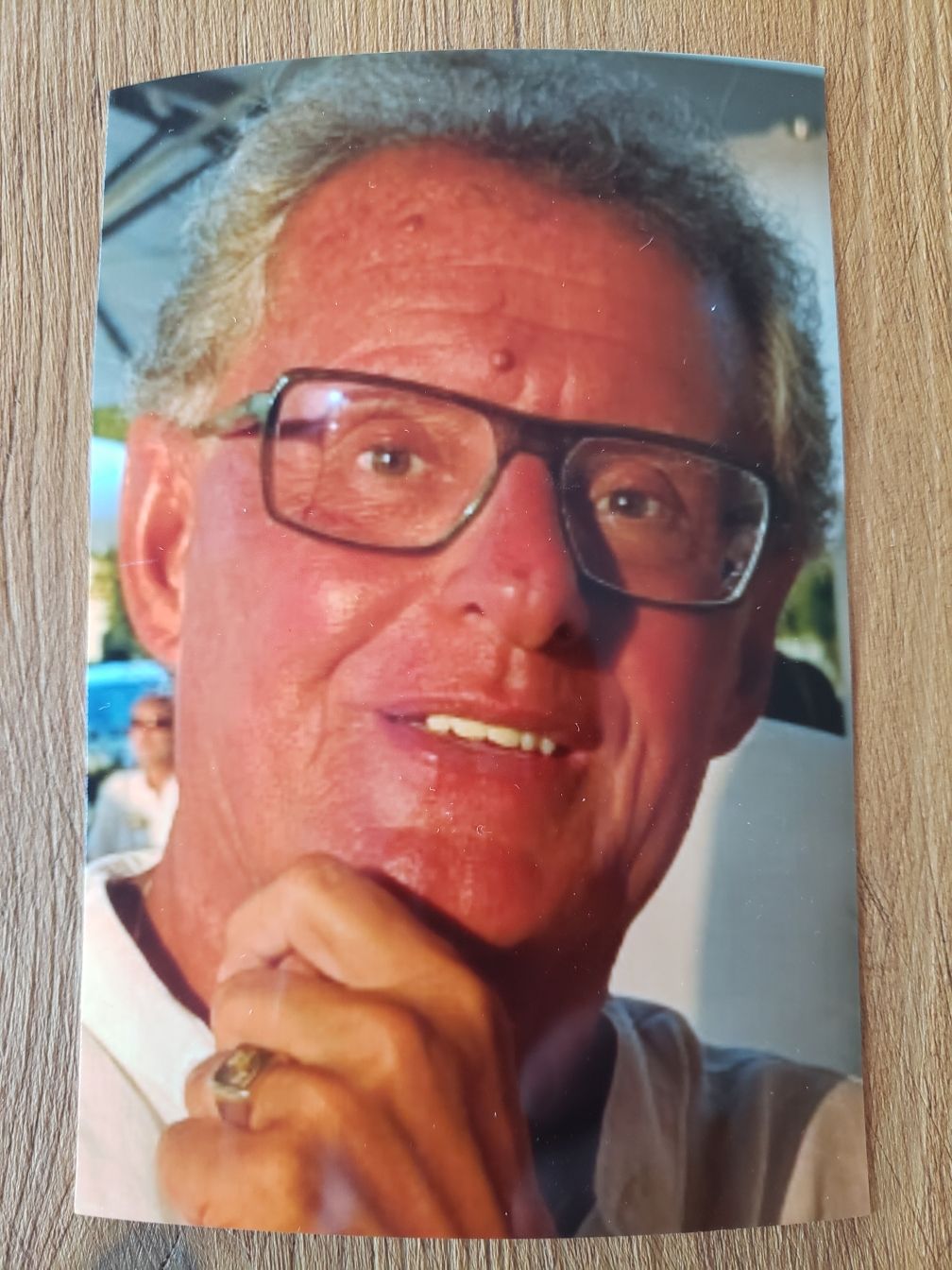 Un homme souriant aux cheveux et à la barbe grisonnants, vêtu d'un costume claire et d'une chemise blanche