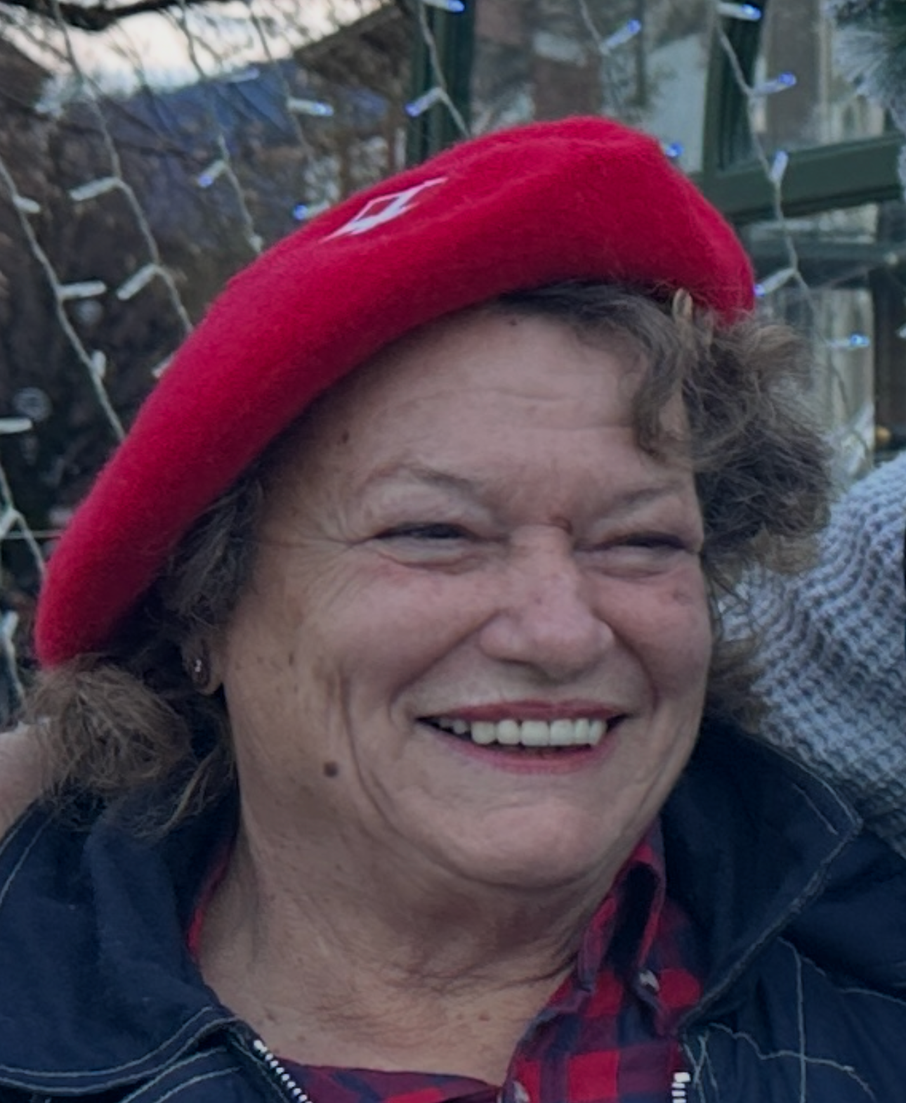 Une femme coiffée d'un béret rouge affiche un large sourire. En extérieur, en journée.