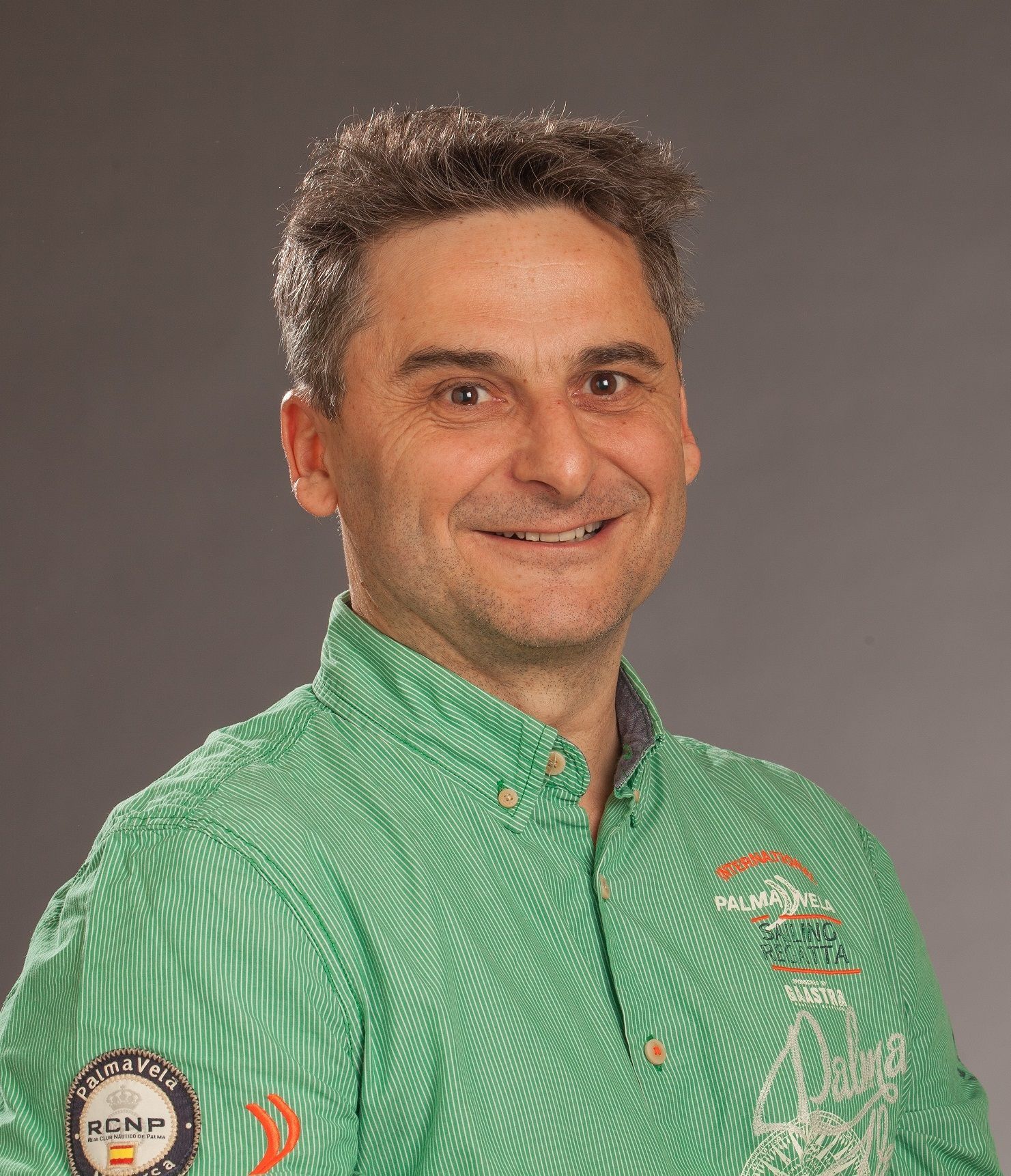 Un homme en chemise verte sourit à l'objectif, sur fond gris.