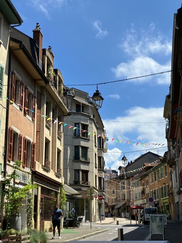Rue d'une ville européenne avec des bâtiments, des guirlandes lumineuses et un ciel bleu.