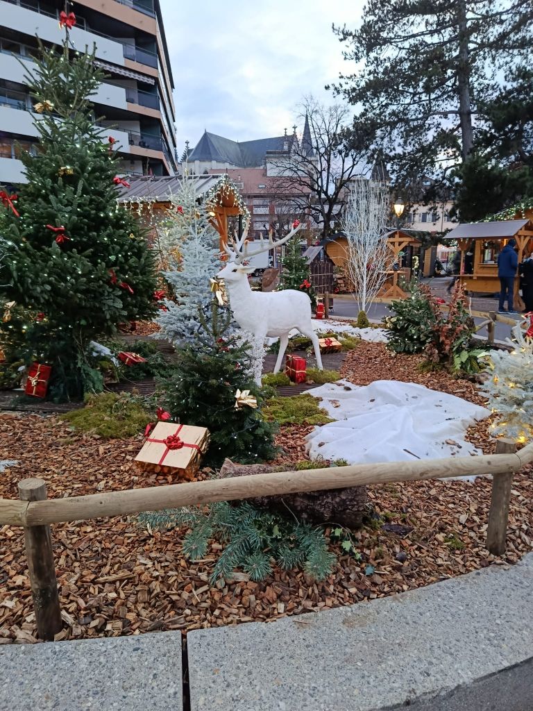 Scène de marché de Noël avec une statue de cerf blanc et des arbres décorés.
