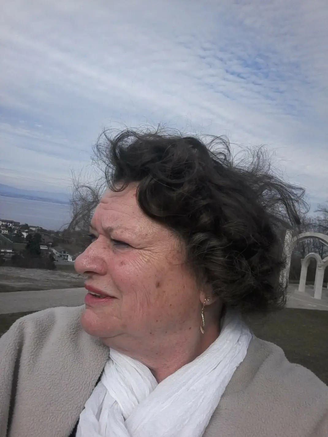 Une femme coiffée d'un béret rouge affiche un large sourire. En extérieur, en journée.