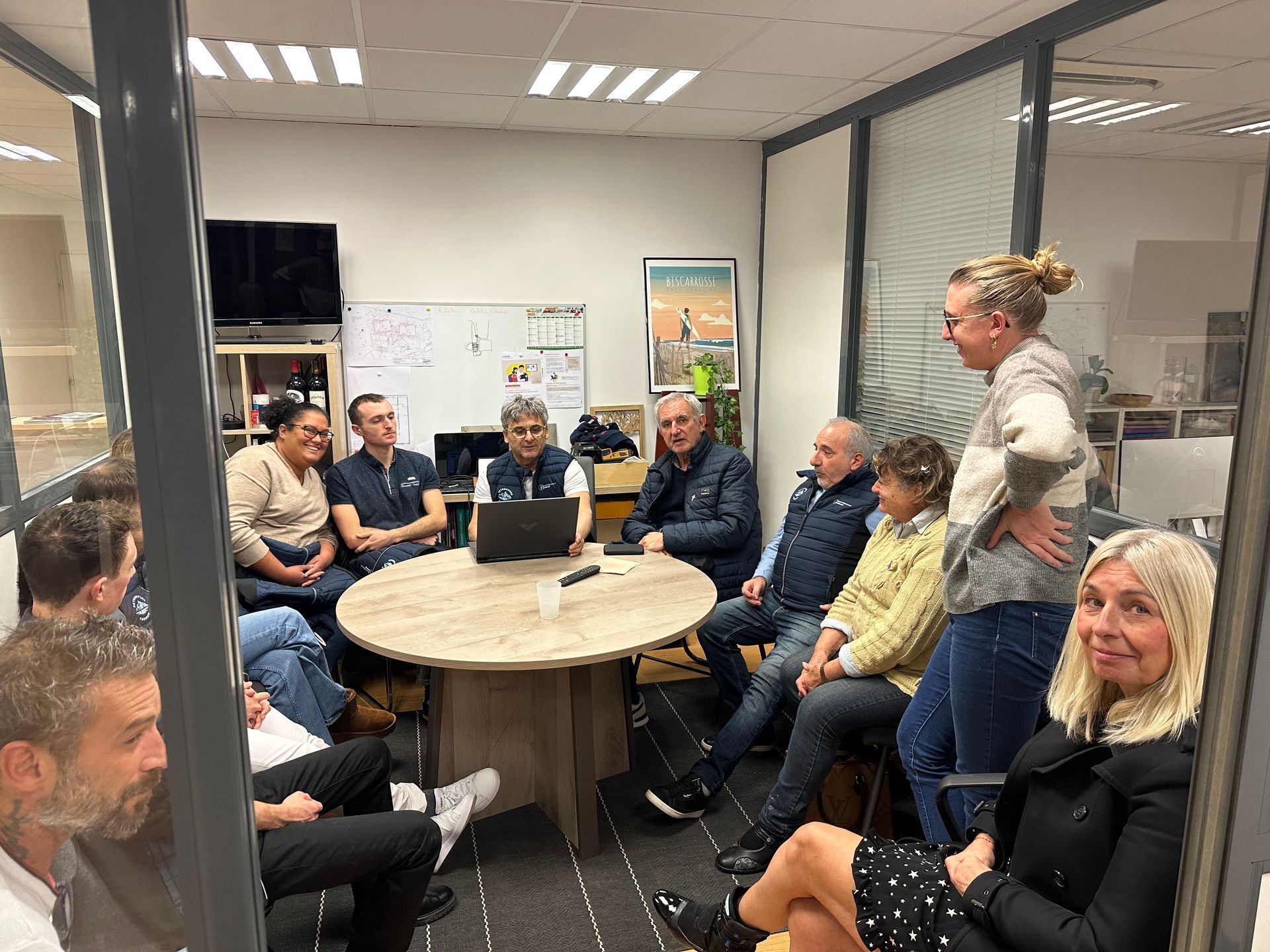 Des personnes réunies dans une salle de réunion, rassemblées autour d'une table ronde, regardent un écran d'ordinateur.
