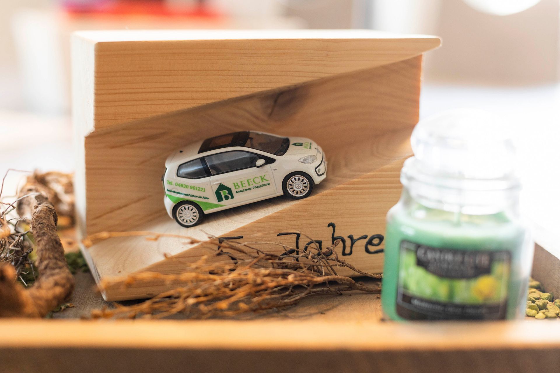 Ein Spielzeugauto steht auf einem Holzklotz neben einer Kerze.