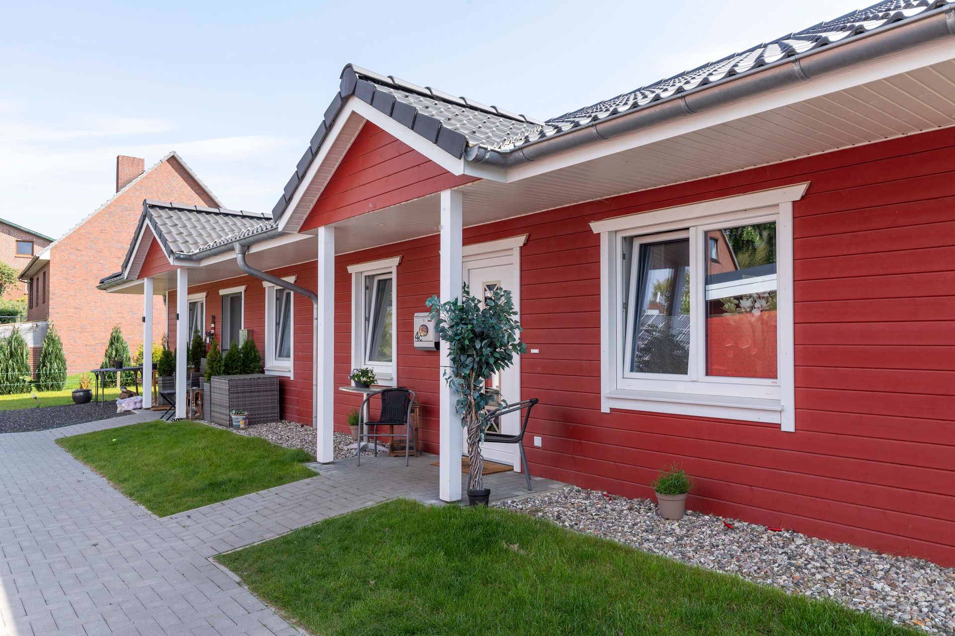 Ein rotes Haus mit einer Veranda und einem Rasen davor.