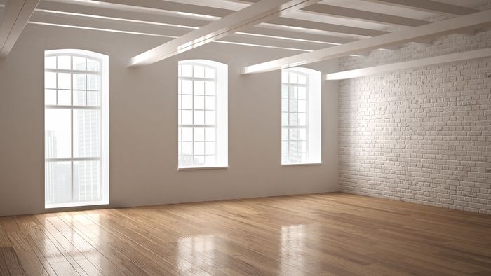 Una habitación vacía con suelo de madera y tres ventanas.