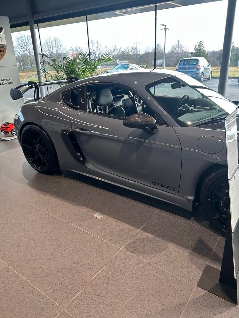 Voiture de sport grise exposée à l'intérieur d'une salle d'exposition avec de grandes baies vitrées.