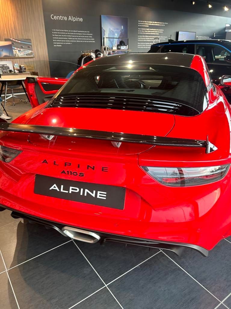 Voiture de sport Alpine rouge exposée dans un showroom, vue arrière avec toit noir et logo ALPINE