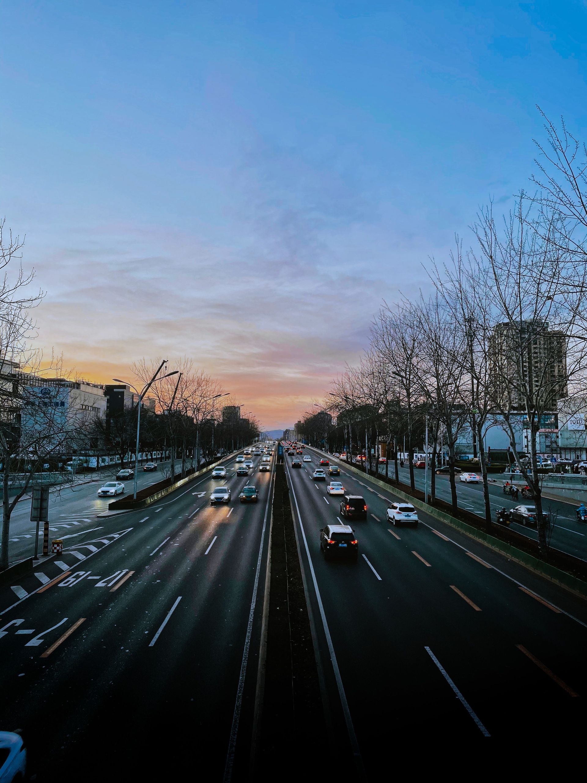 Un boulevard animé au crépuscule, avec des voitures circulant sous un ciel rose bleuâtre.