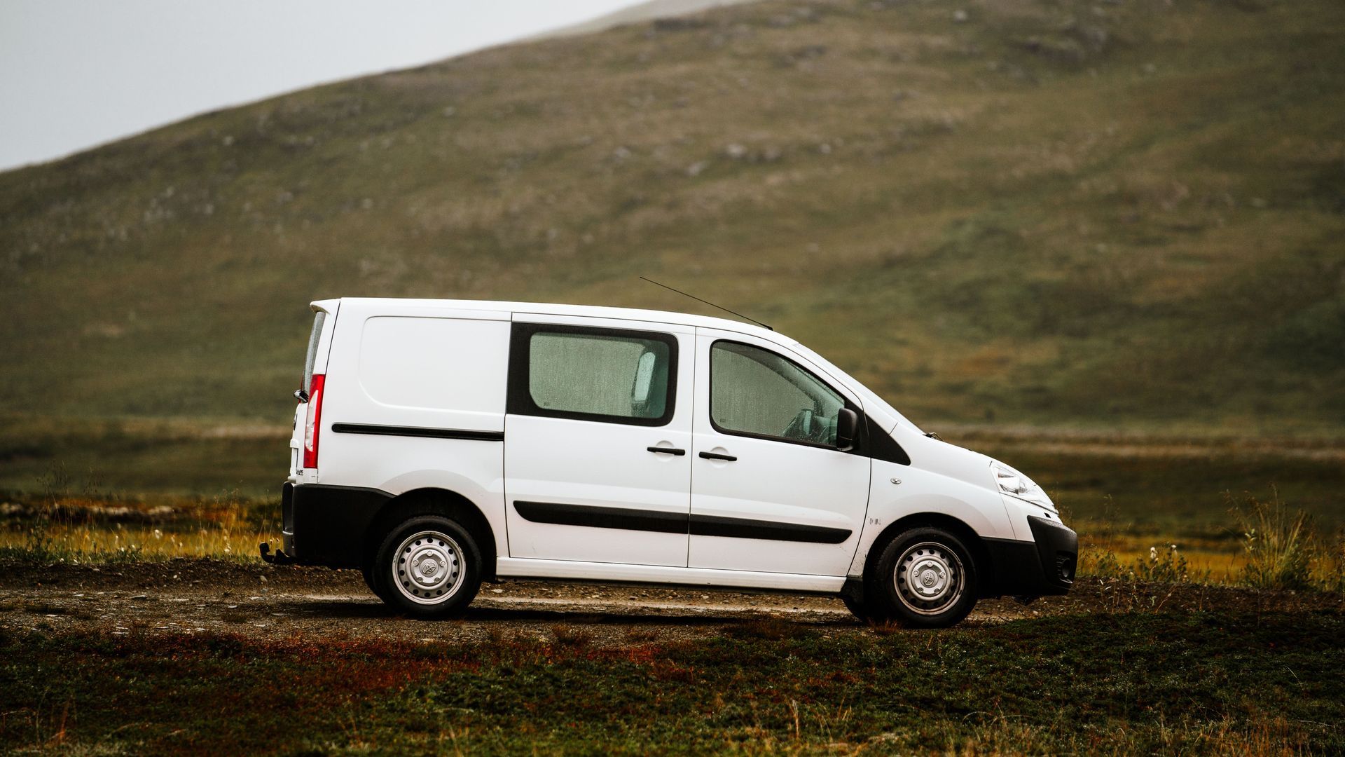 Une camionnette blanche roule sur une route de montagne sous un ciel couvert.