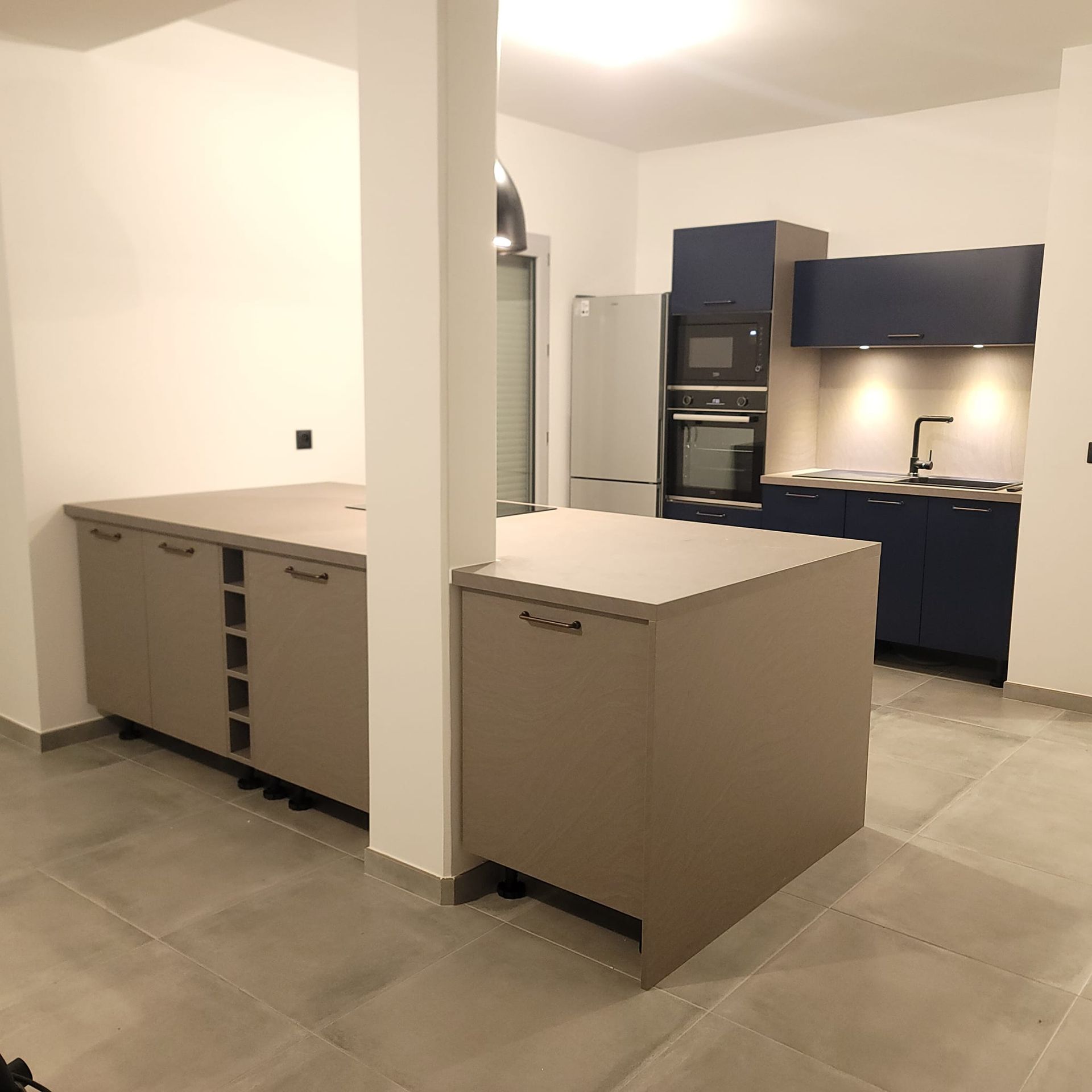 Cuisine moderne avec un îlot aux tons clairs, un pilier structurel et des armoires bleu marine.