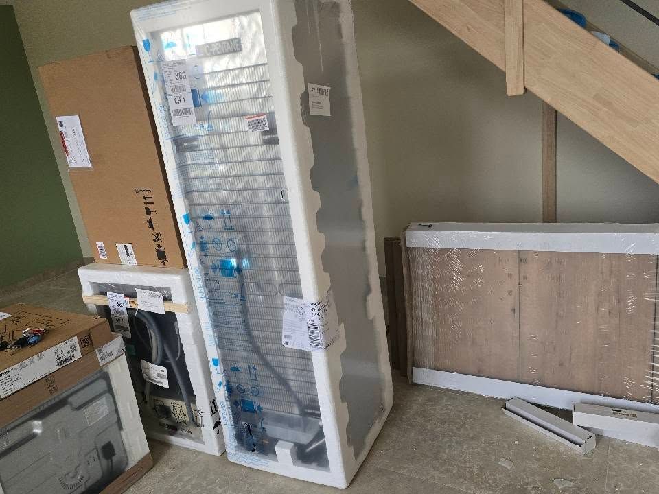 Des cartons d'électroménager et de meubles sont entreposés dans une pièce sous un escalier.