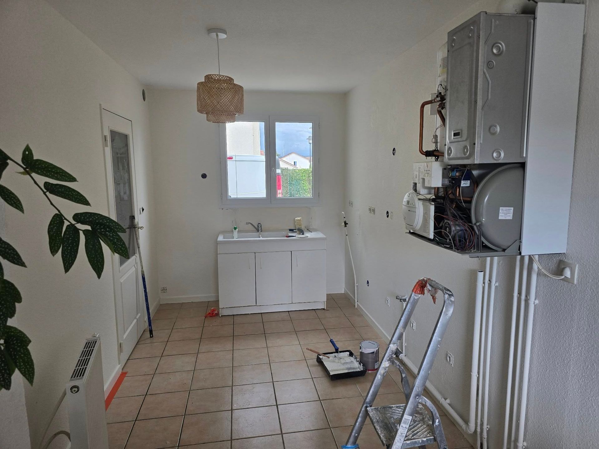 Une pièce meublée avec parcimonie, aux murs blancs avec un évier de cuisine et une chaudière murale aux tuyaux apparents.