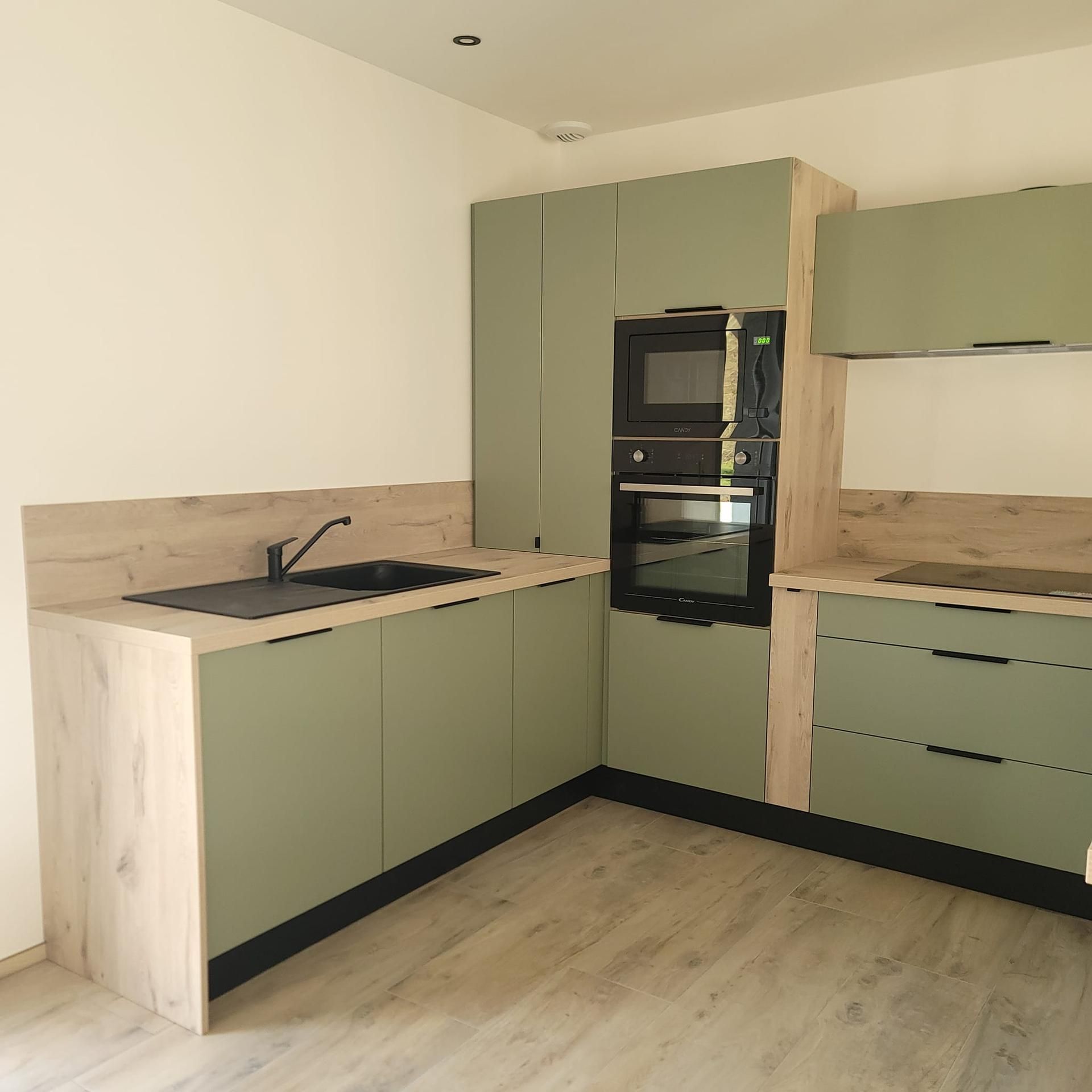 Une cuisine en forme de L avec des armoires vert sauge, des comptoirs et une crédence en bois clair.