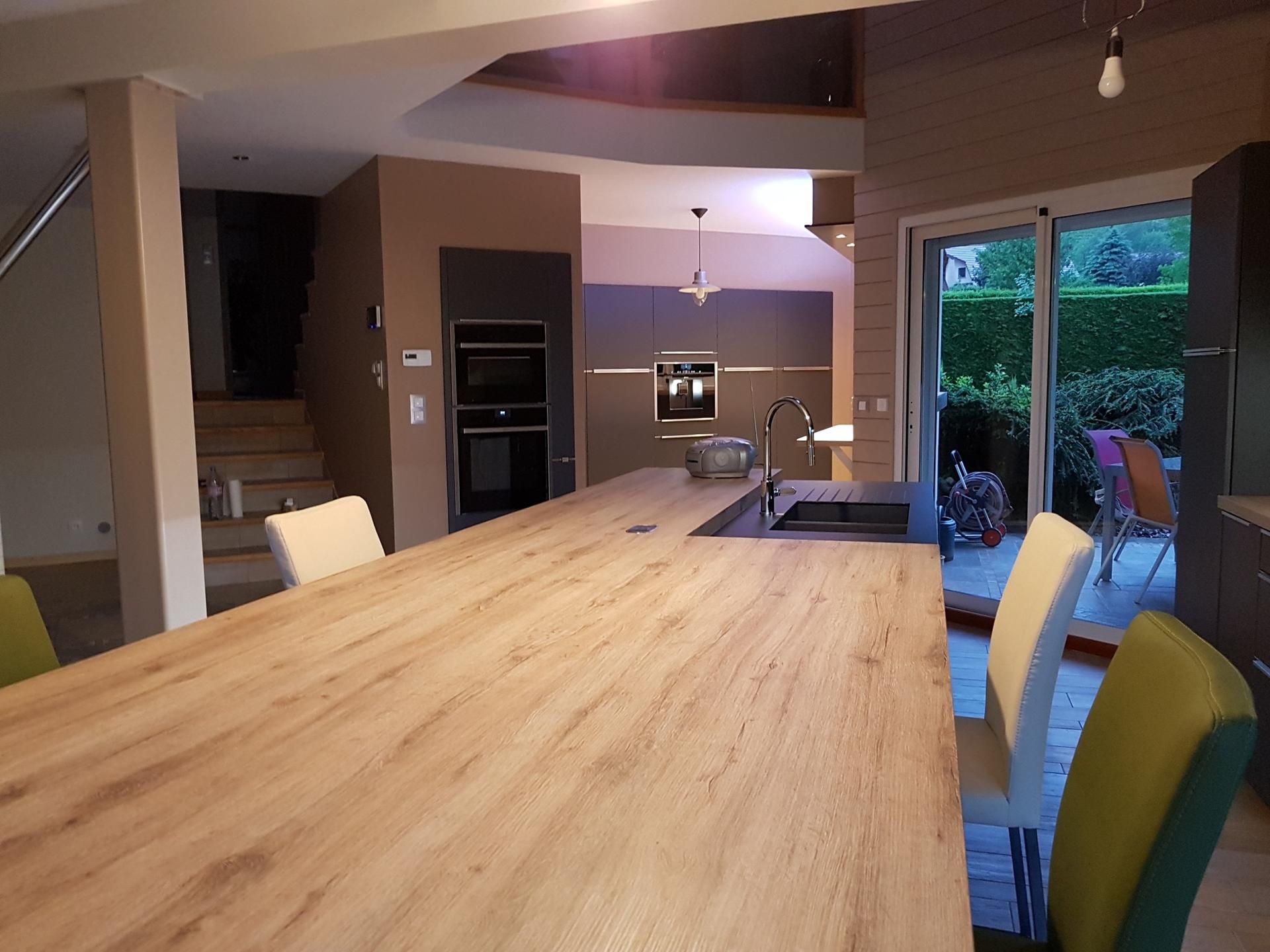 Une cuisine moderne comprend un grand îlot en bois avec un évier, des chaises blanches et vertes, et un mur de fond.