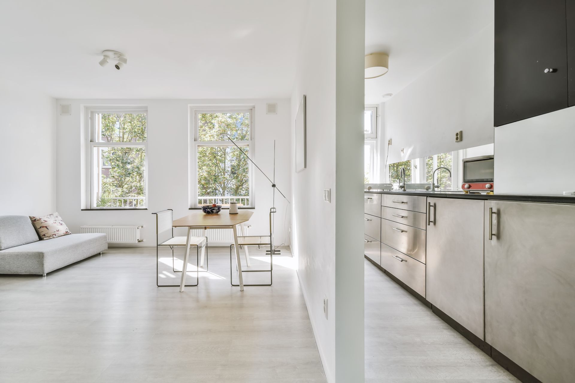 Un salon lumineux à aire ouverte avec un canapé gris, une table à manger et une cuisine moderne aux meubles clairs.