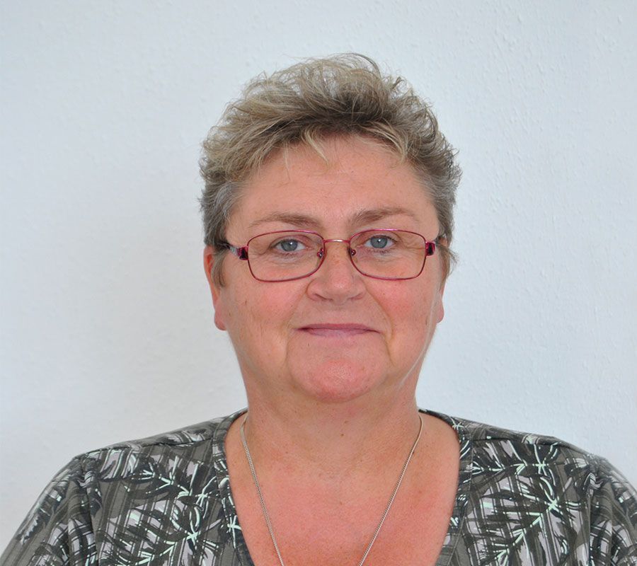 Frau mit Brille und kurzen Haaren, lächelnd, gemustertes Hemd tragend.