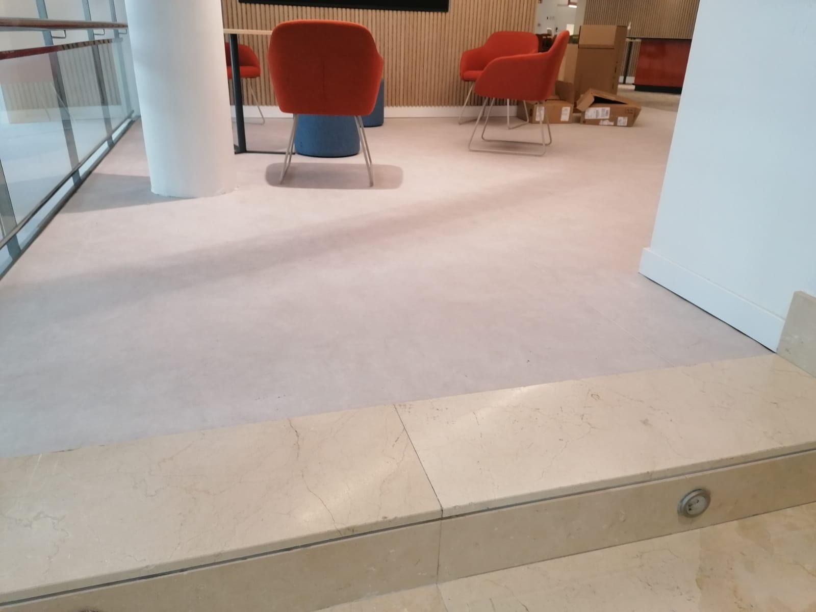 Área alfombrada de color rosa claro con sillas naranjas, una columna y una repisa de mármol.