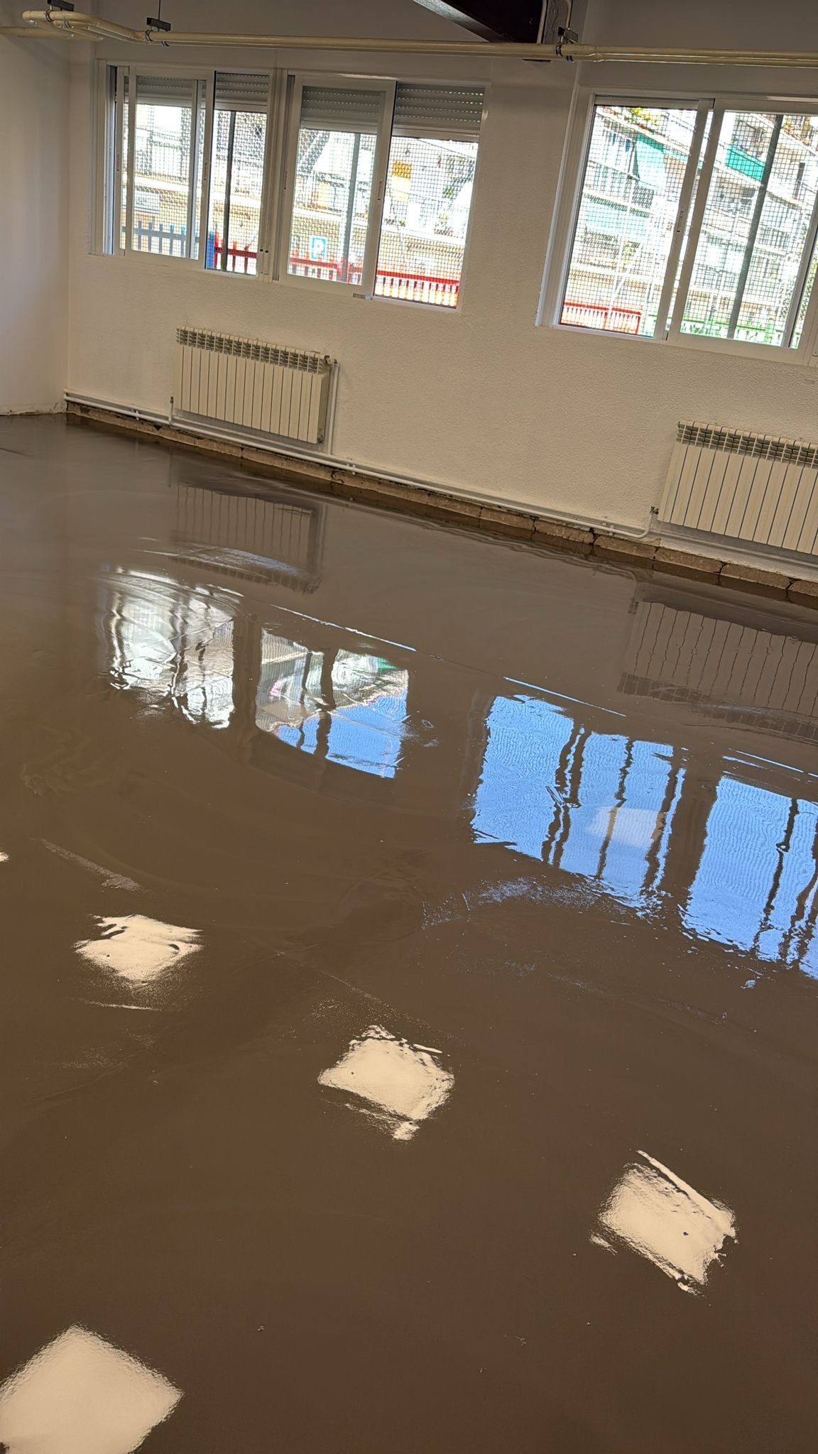 Habitación con suelo nuevo, con una superficie gris brillante que refleja la luz natural de varias ventanas. 