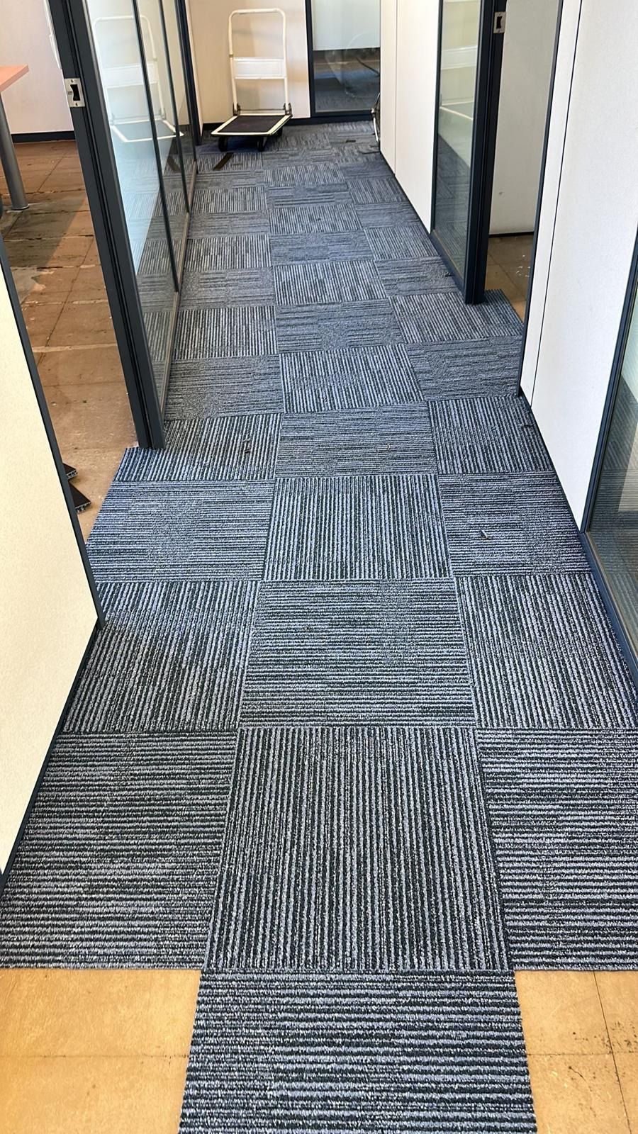 Pasillo con baldosas de moqueta con dibujos azules entre paredes de cristal y color beige.