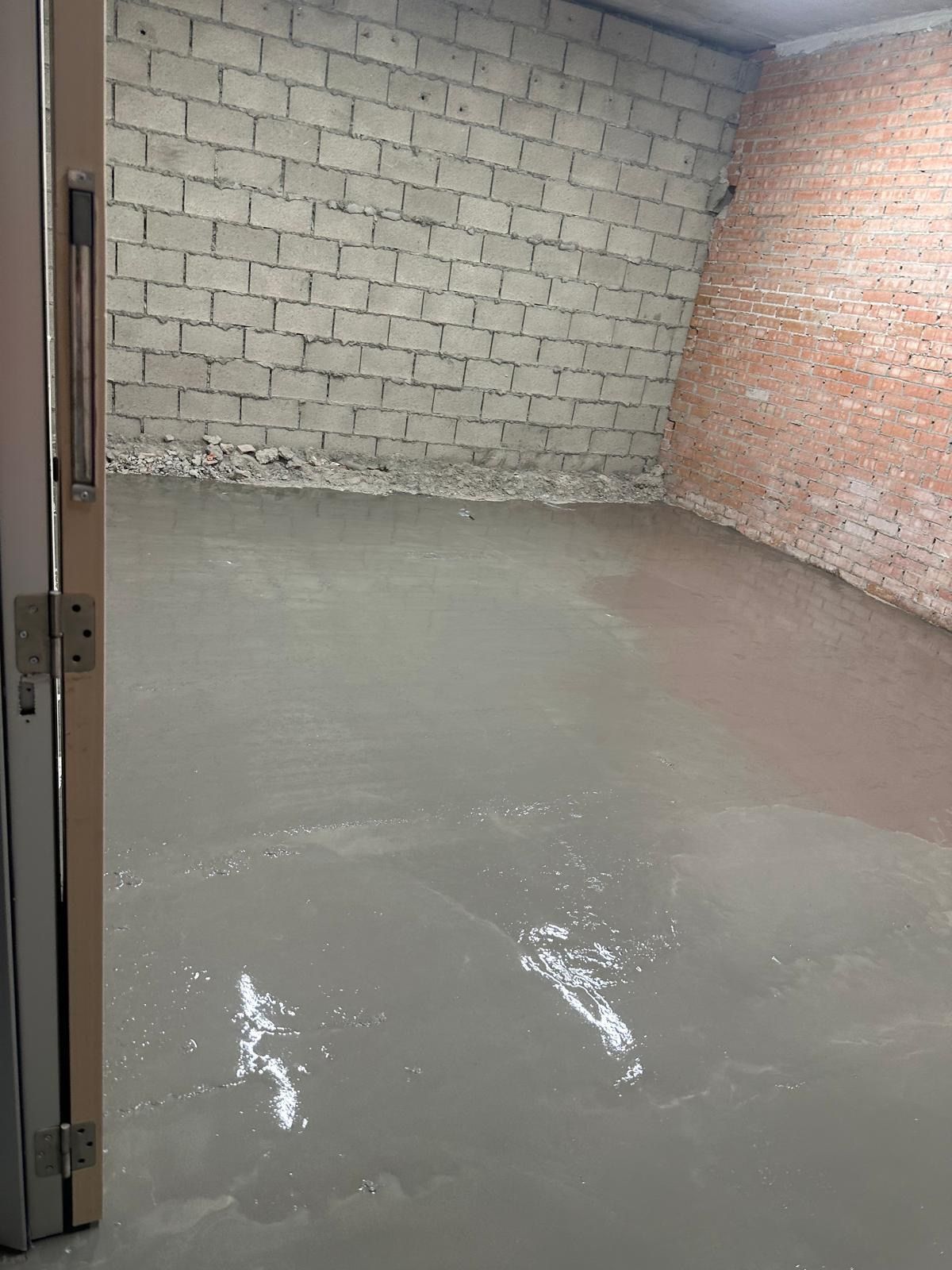 Habitación con suelo de cemento gris y paredes de ladrillo/bloque. Marco de puerta en primer plano.