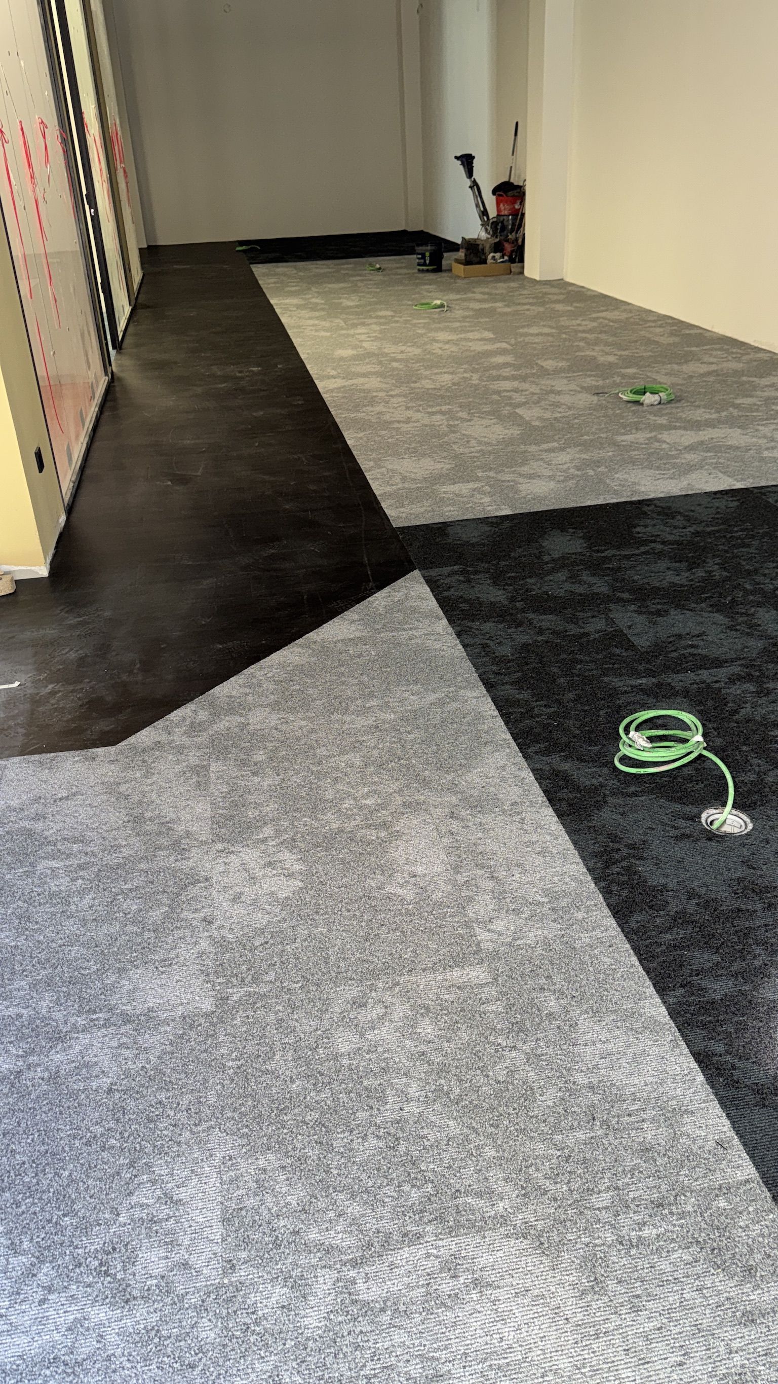 Habitación con losetas de alfombra gris y negra, parcialmente instaladas.