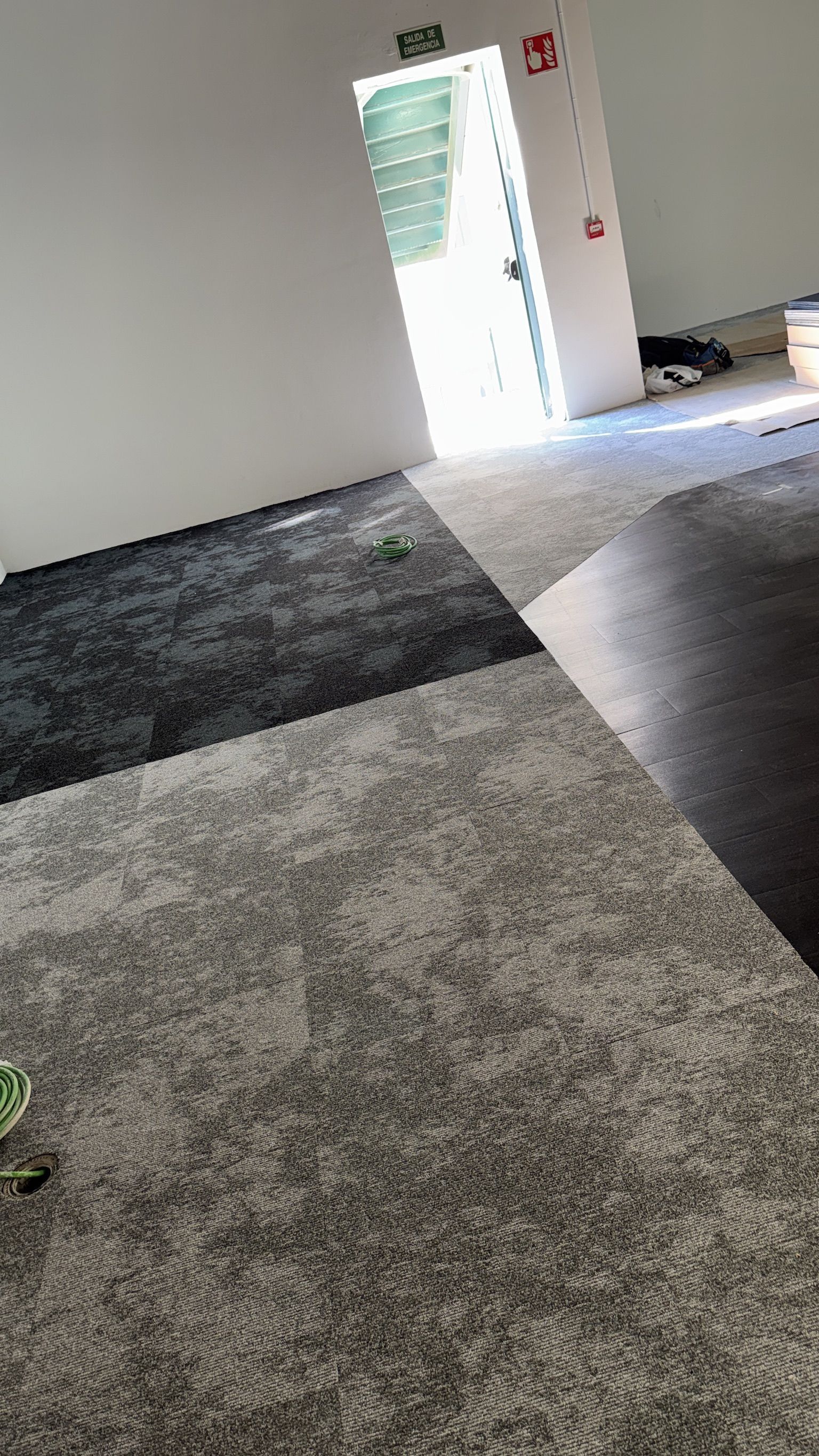 Habitación con suelo gris, negro y imitación madera; puerta abierta con luz brillante; paredes blancas.