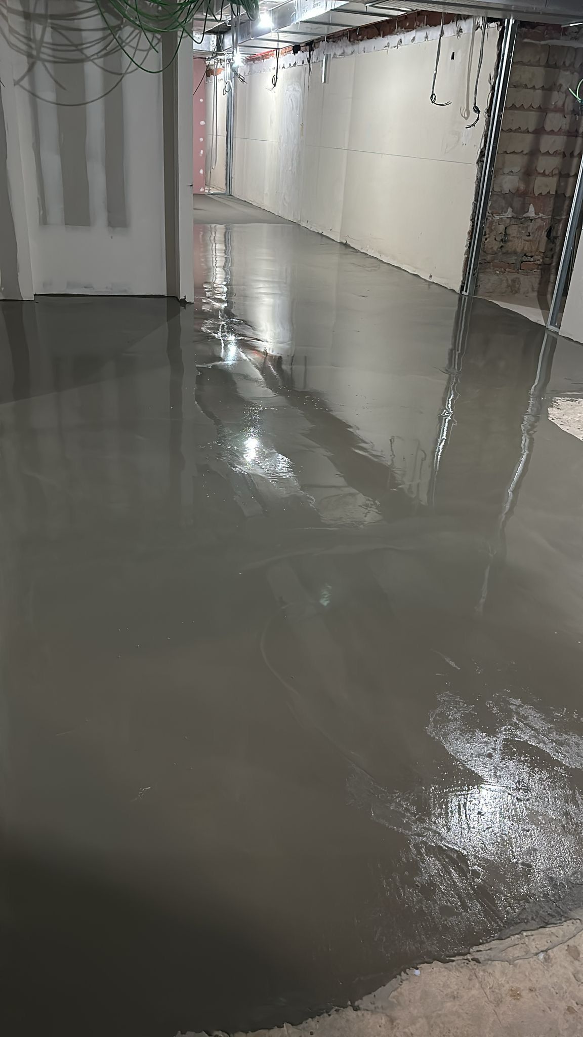 Piso de concreto húmedo en un sitio de construcción, con paredes y una escalera visibles.