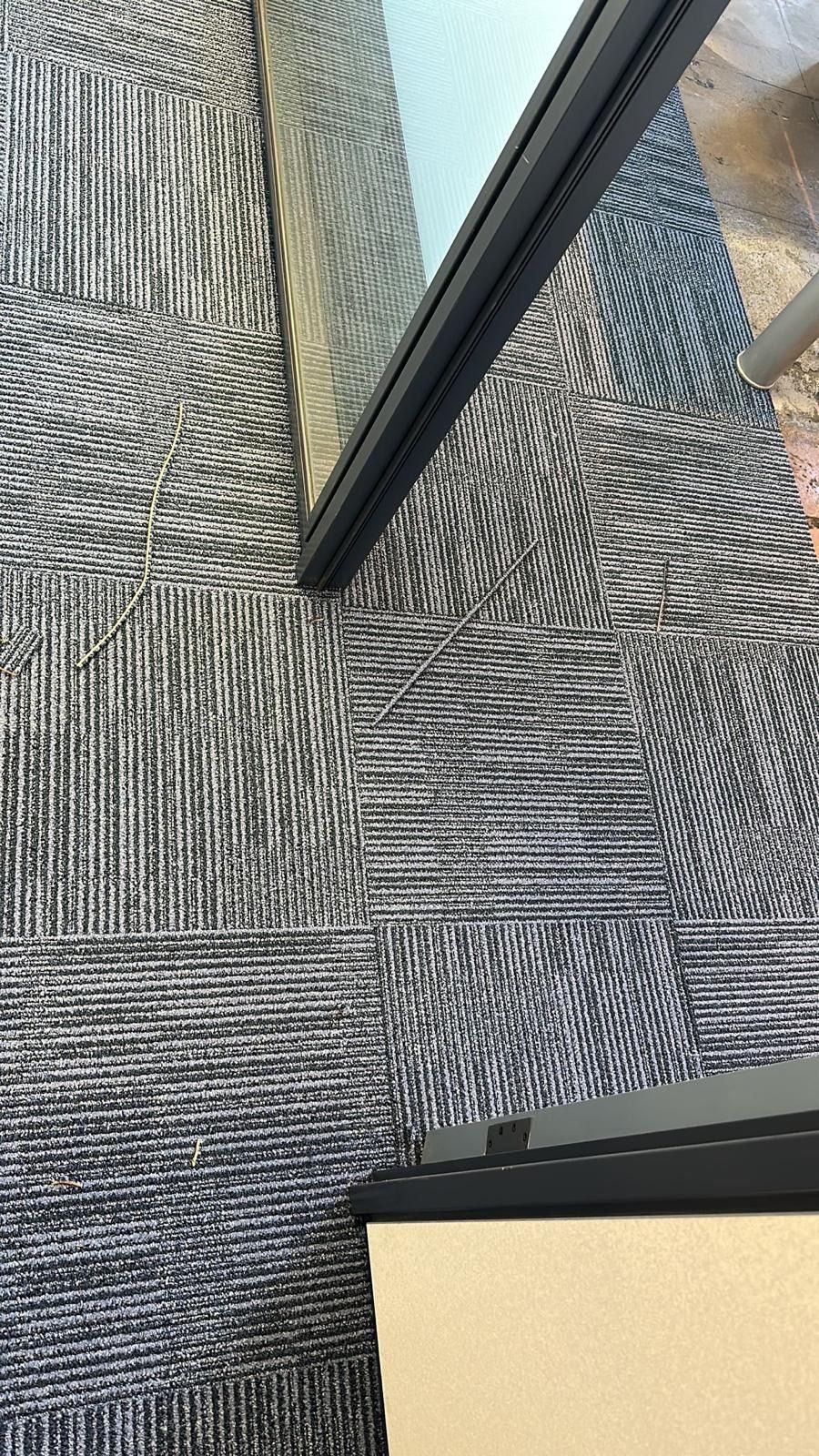 Panel con marco negro sobre losetas de alfombra con estampado gris.