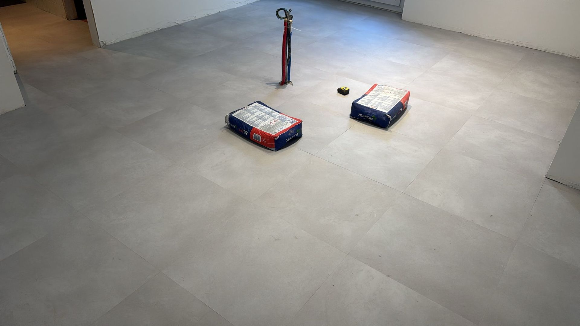 Suelo de baldosas grises con dos cajas y una herramienta roja alta en una habitación vacía.