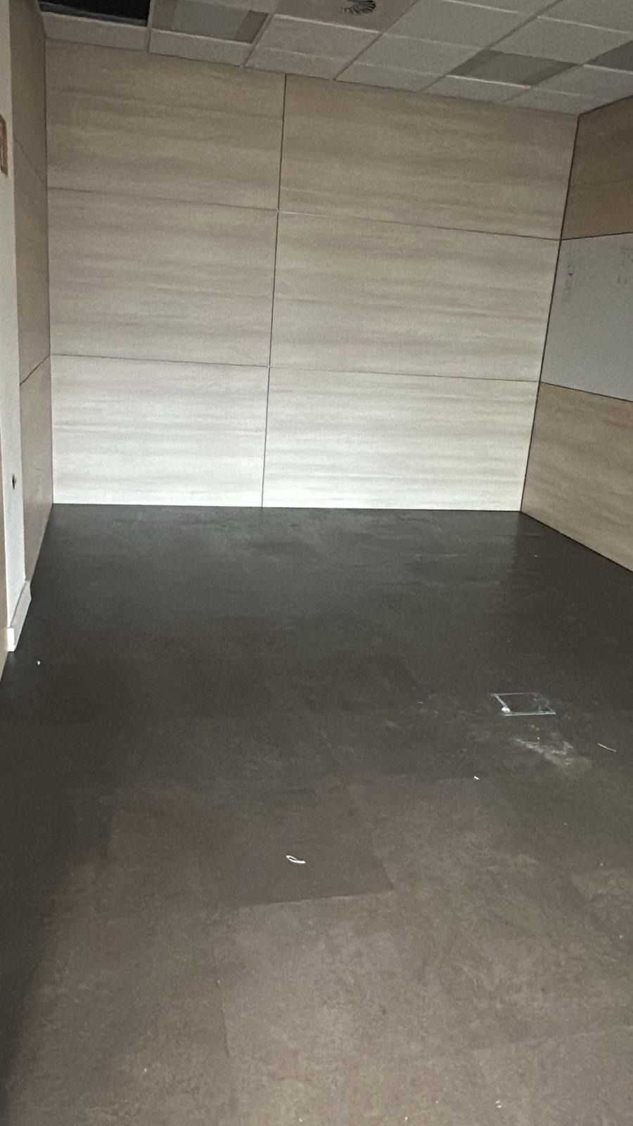 Habitación vacía con suelo gris oscuro y pared de azulejos beige claro.