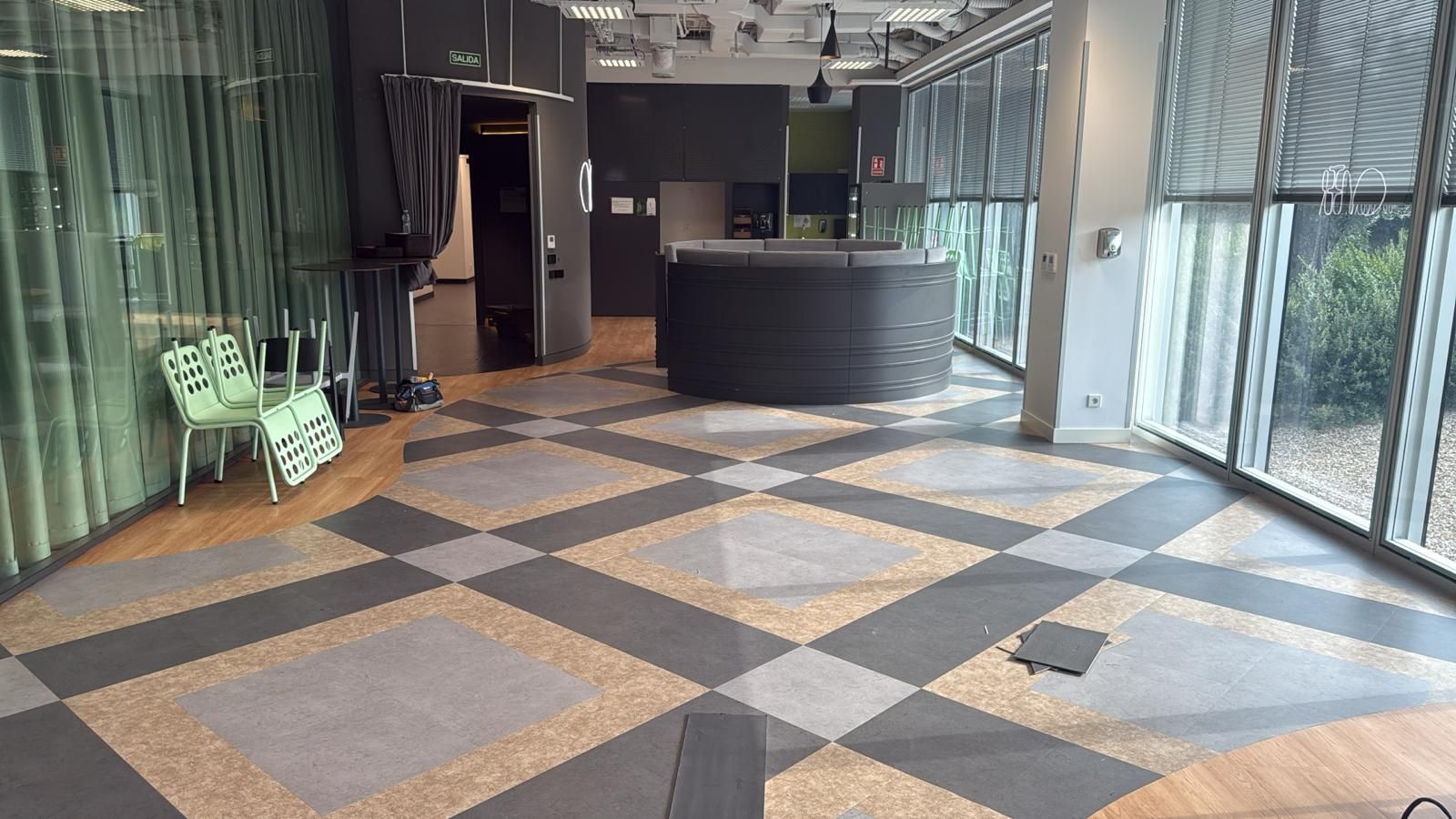 Vestíbulo de oficina abierto con suelo con diseño geométrico, escritorio redondo y grandes ventanales.