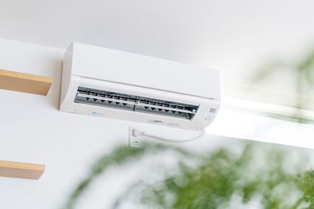 Climatiseur mural blanc près d'une fenêtre avec un flou extérieur vert doux.