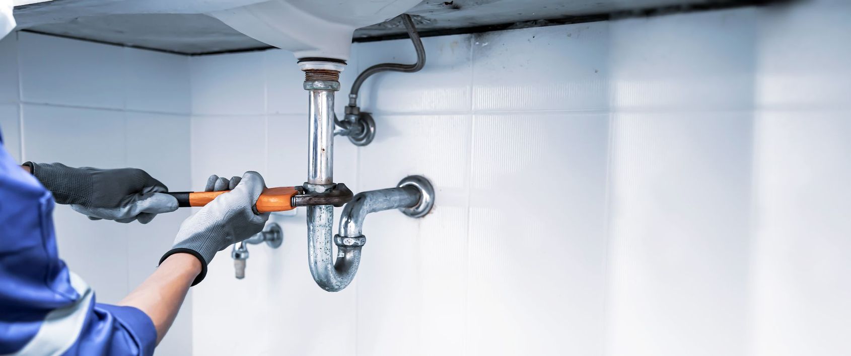Une personne vaporise du désinfectant sur la tuyauterie d'un lavabo dans une pièce blanche.