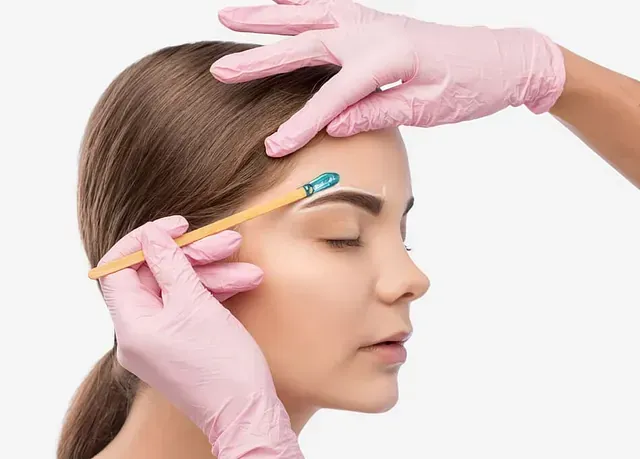 Una mujer se pinta las cejas con una mujer que lleva guantes rosas.