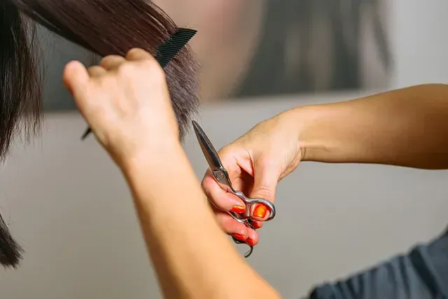 Una mujer se está cortando el pelo con unas tijeras por un peluquero.