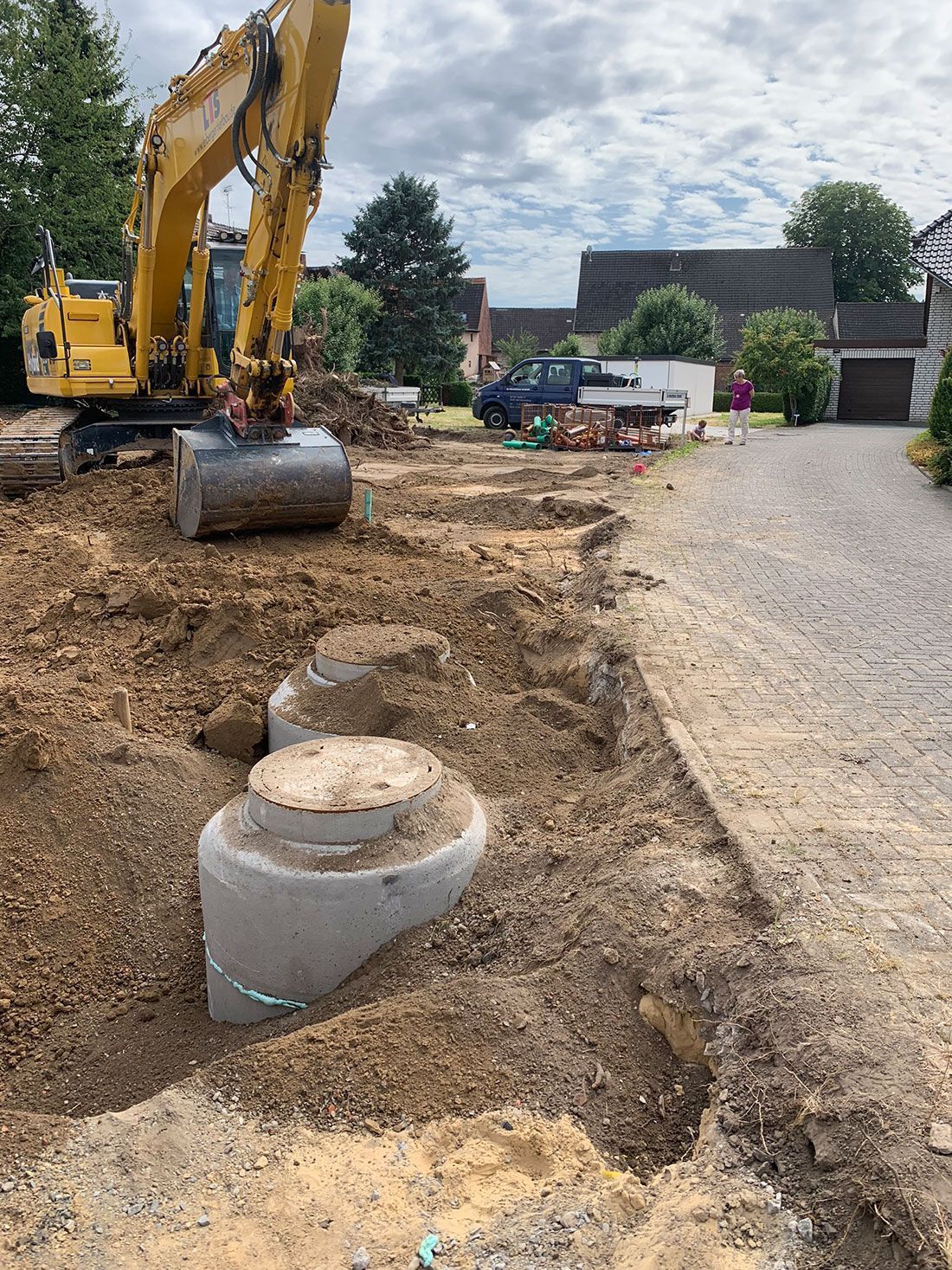 Ein gelber Bagger gräbt vor einem Haus ein Loch in die Erde.