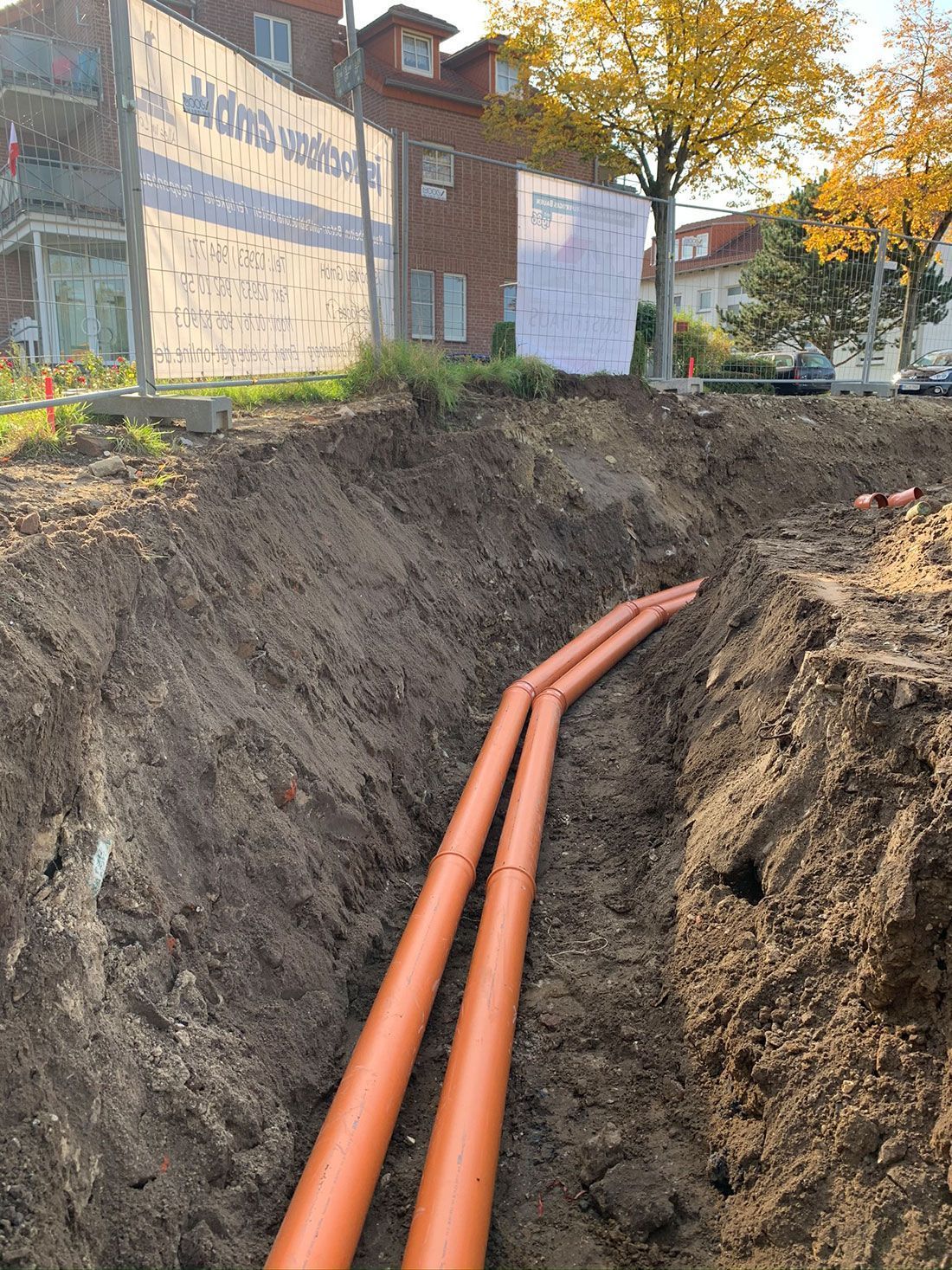 In einem Loch im Boden werden zwei orangefarbene Rohre installiert.