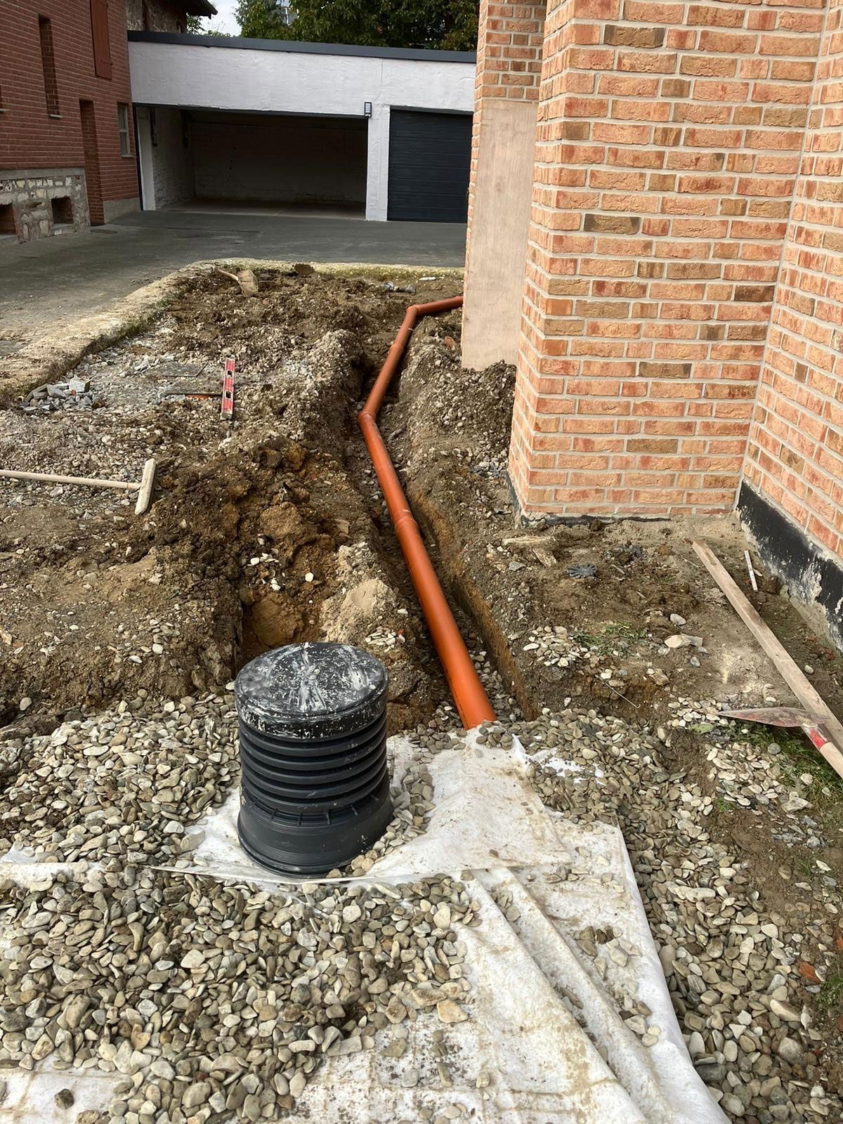 Vor einem Backsteingebäude wird im Boden ein Abflussrohr installiert.