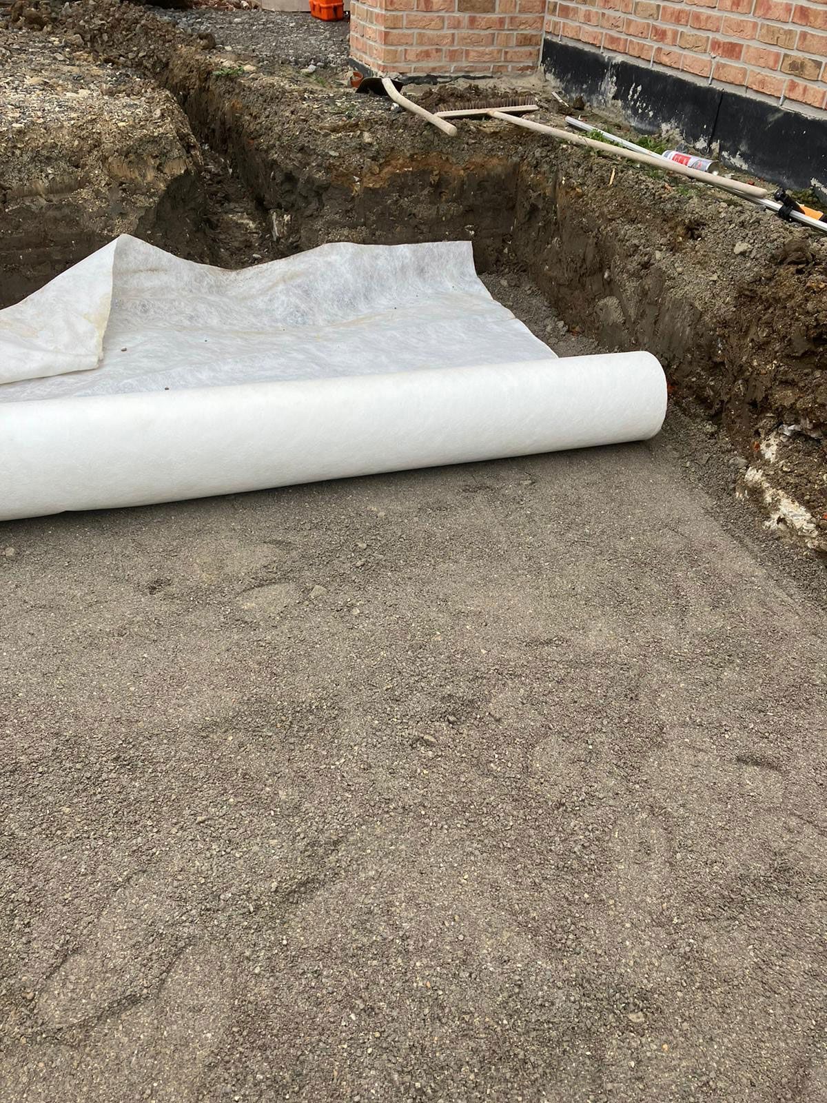 Eine Rolle weißer Plane liegt neben einem Loch auf dem Boden.