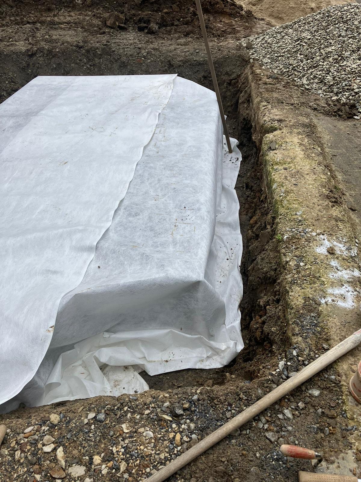 Ein Stück weißes Tuch liegt neben einer Schaufel im Dreck.