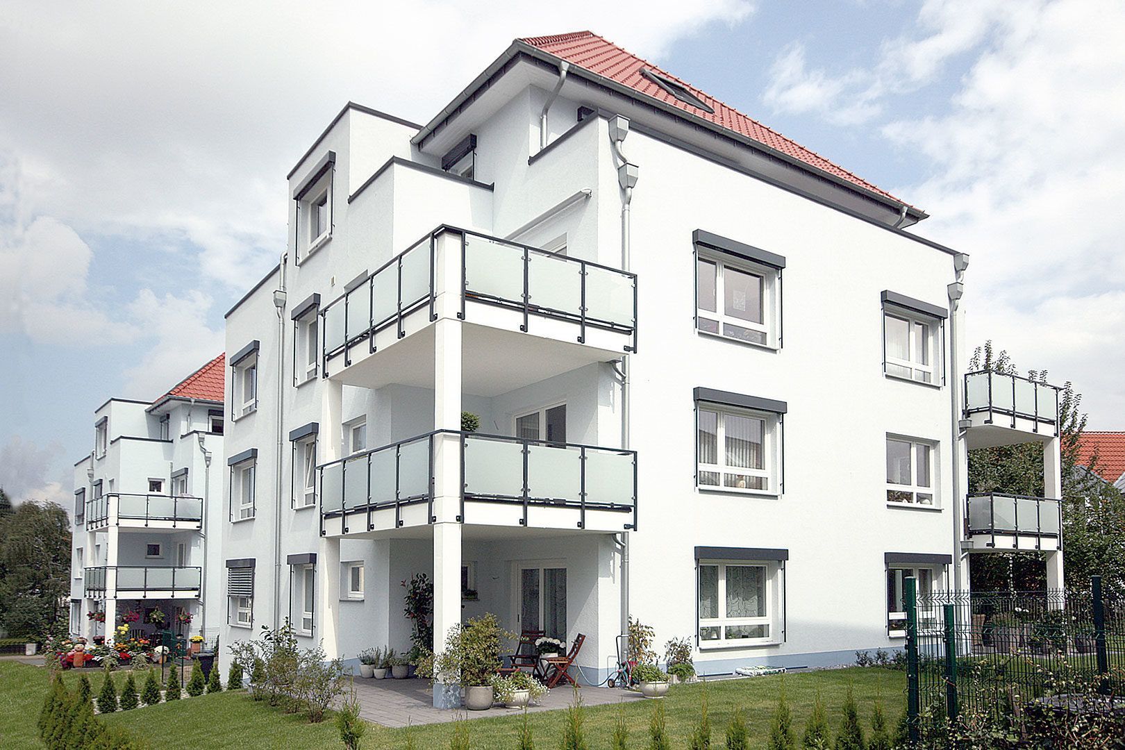 Ein weißes Mehrfamilienhaus mit Balkonen und einem roten Dach