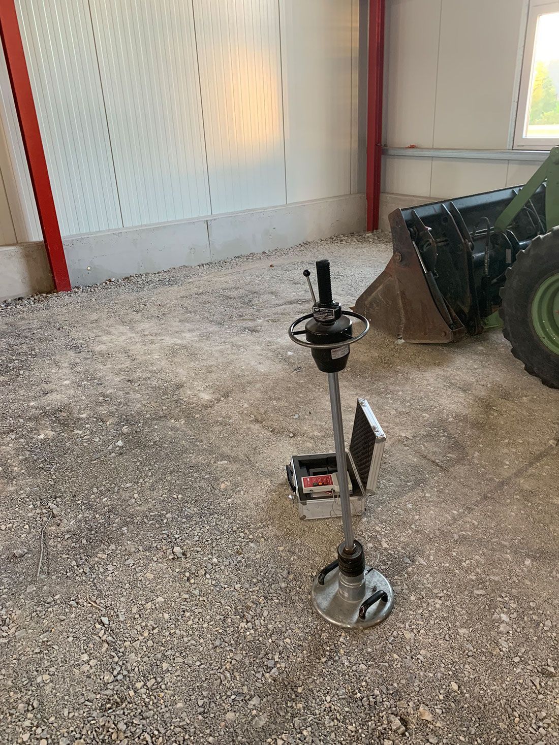 Ein Rasenmäher steht auf einem Kiesboden neben einem Traktor.