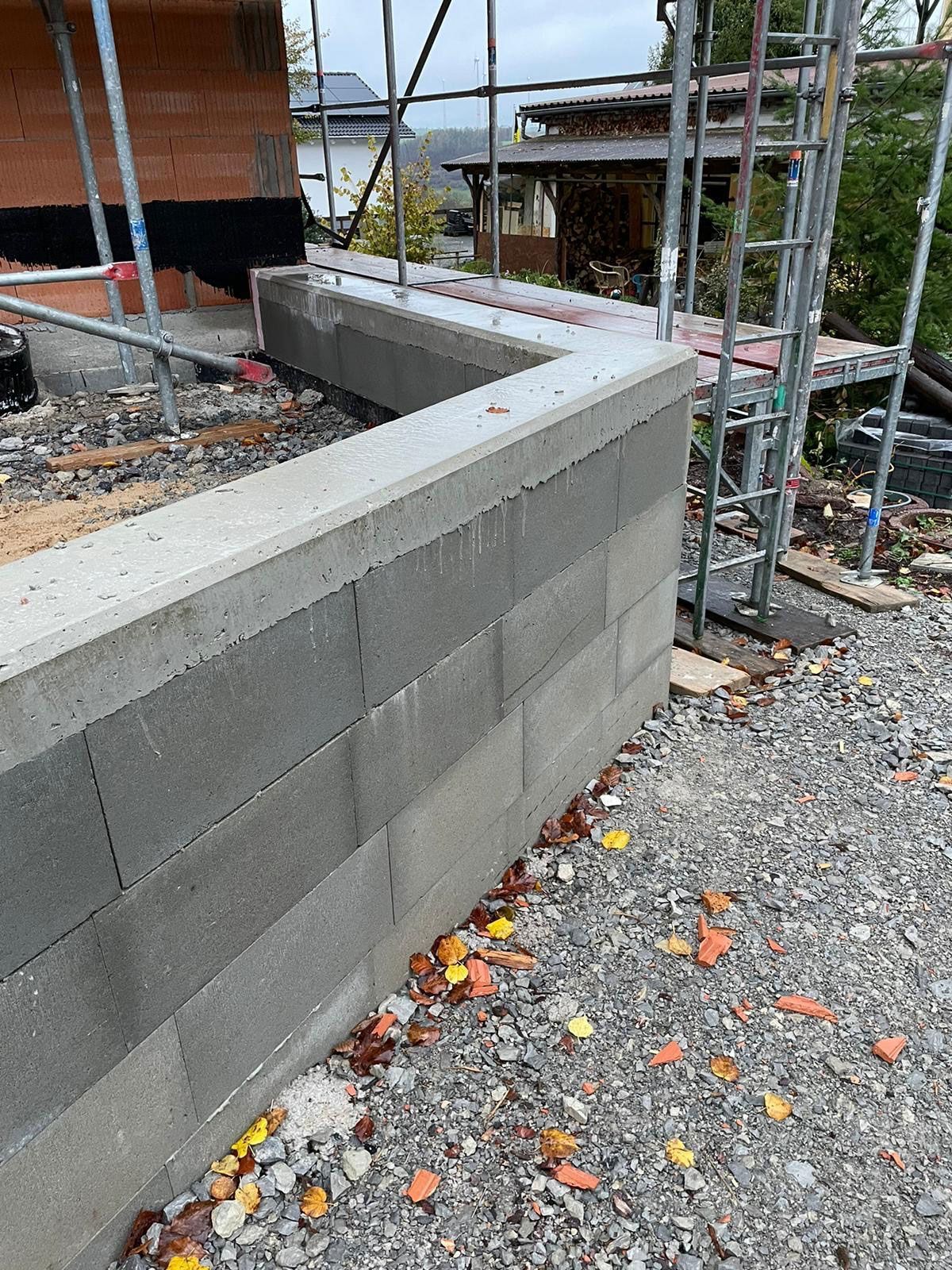 Neben einer Schotterstraße wird eine Backsteinmauer gebaut.