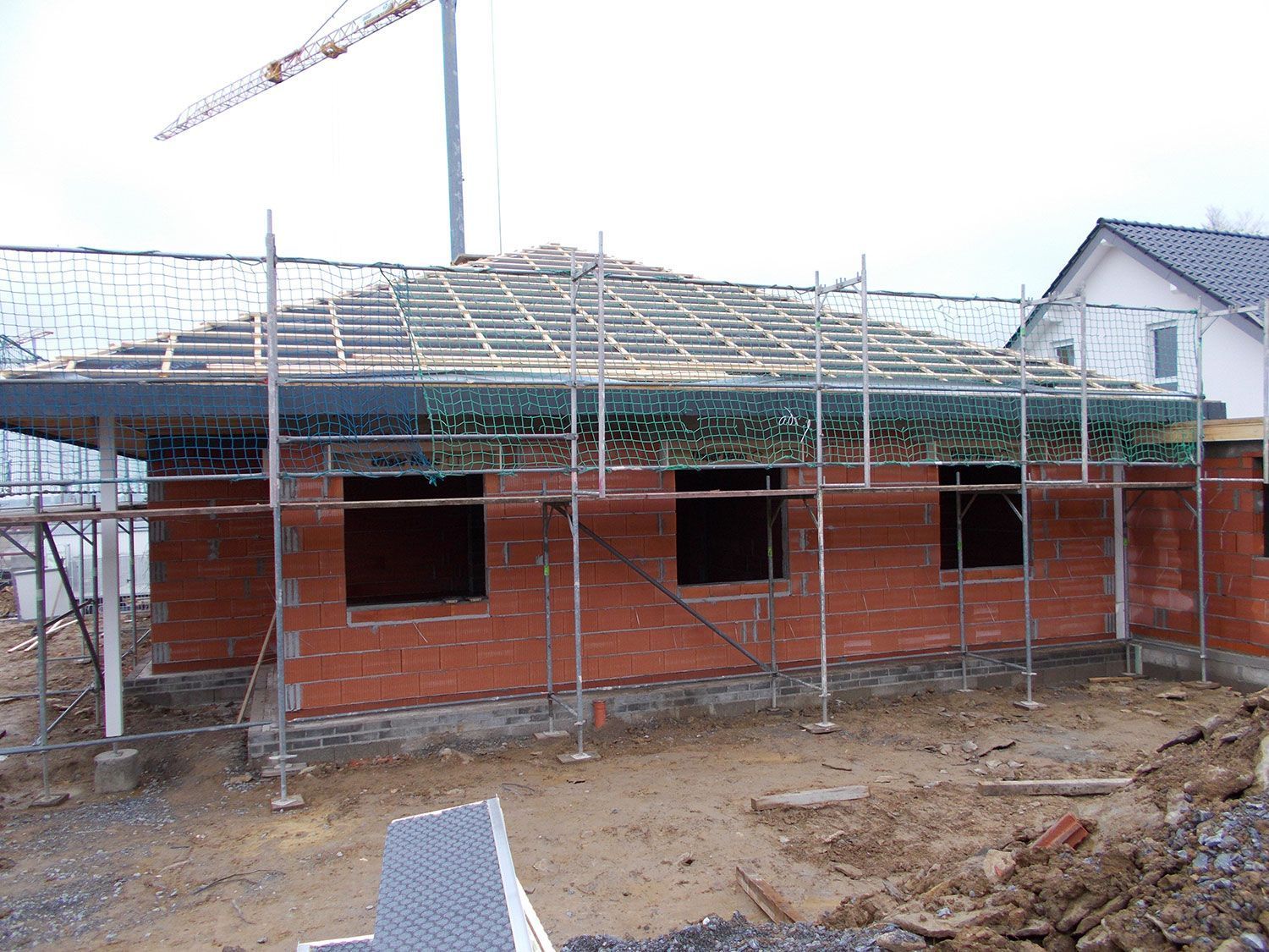 Ein Backsteinhaus wird gebaut, im Hintergrund sind ein Gerüst und ein Kran zu sehen.
