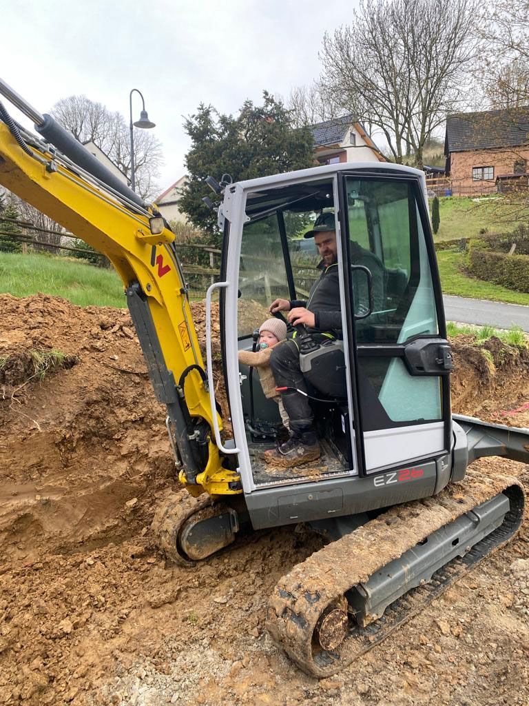 Ein Mann fährt einen gelben Bagger auf einer unbefestigten Straße.