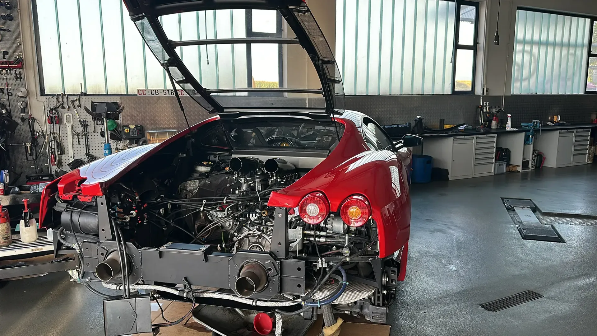 In einer Garage wird an einem roten Sportwagen mit geöffnetem Verdeck gearbeitet.